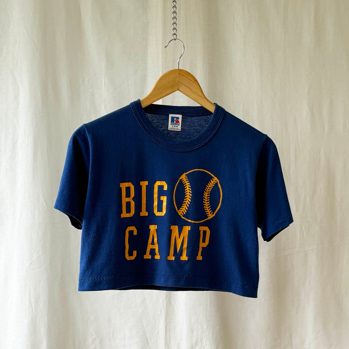 Navy blue t-shirt with 'BIG CAMP' and baseball graphic on a hanger against a white background