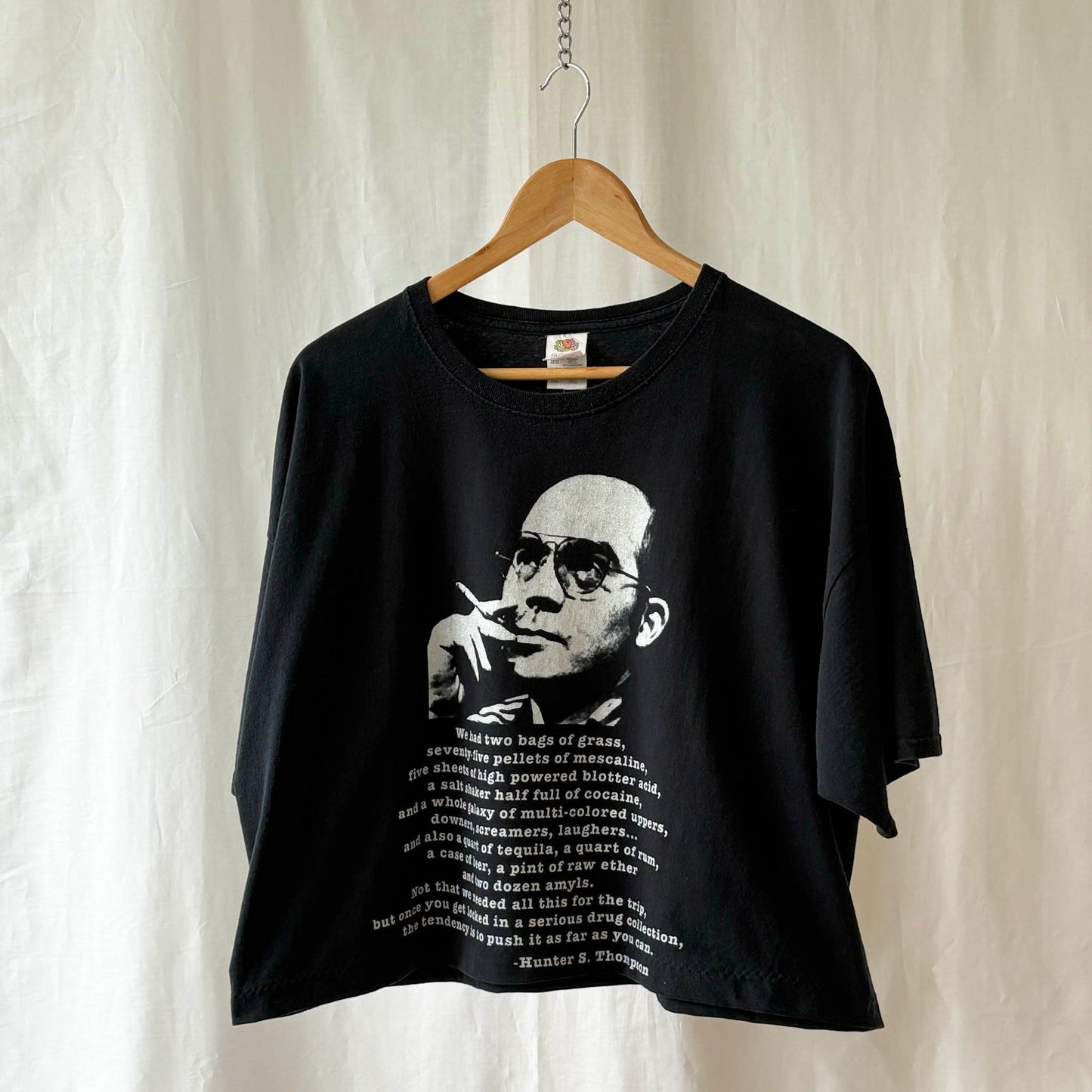 Black t-shirt with a white graphic of Hunter S. Thompson and quote from Fear and Loathing in Las Vagas on a hanger against a white curtain background