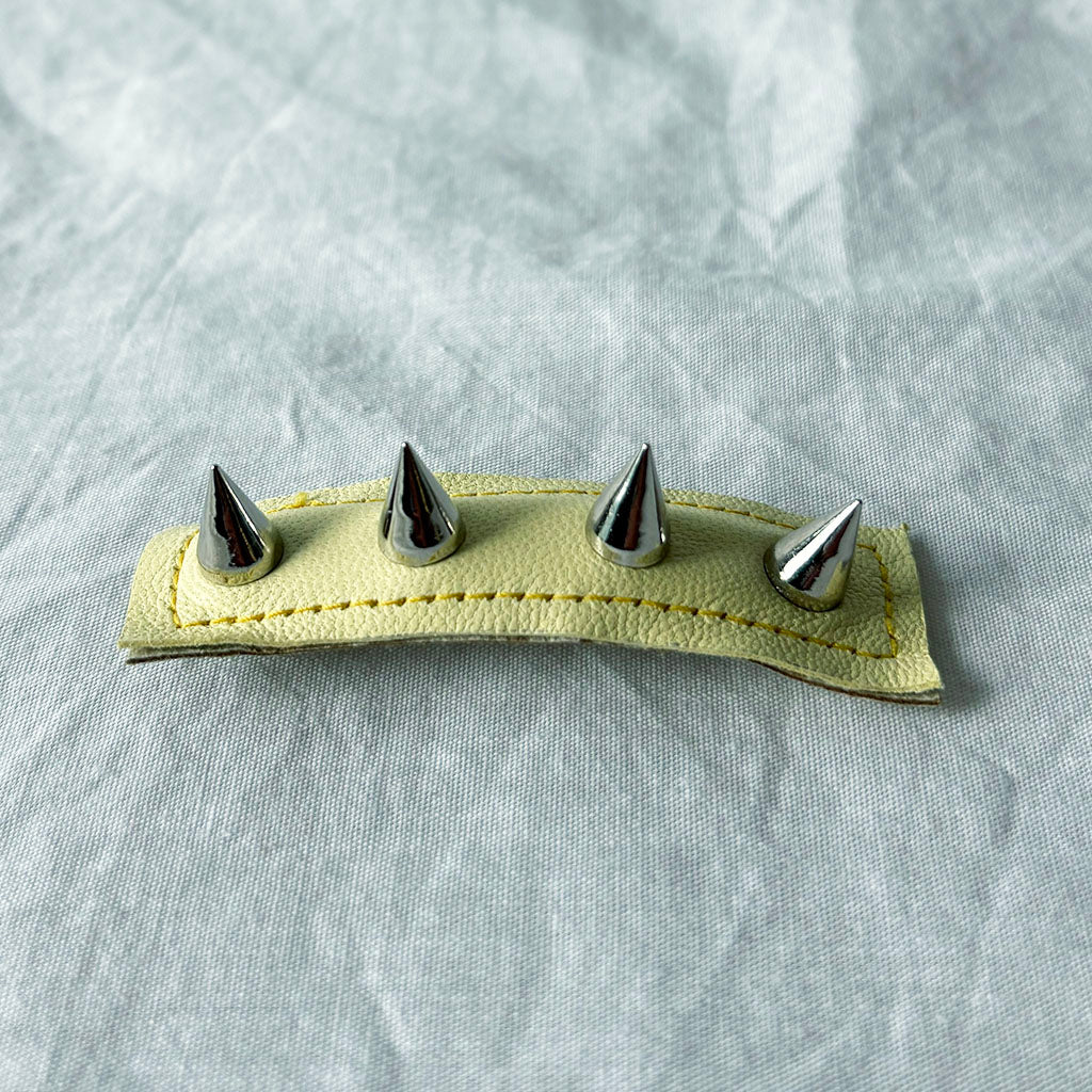 pale yellow leather barrette with four silver spikes on a light gray background