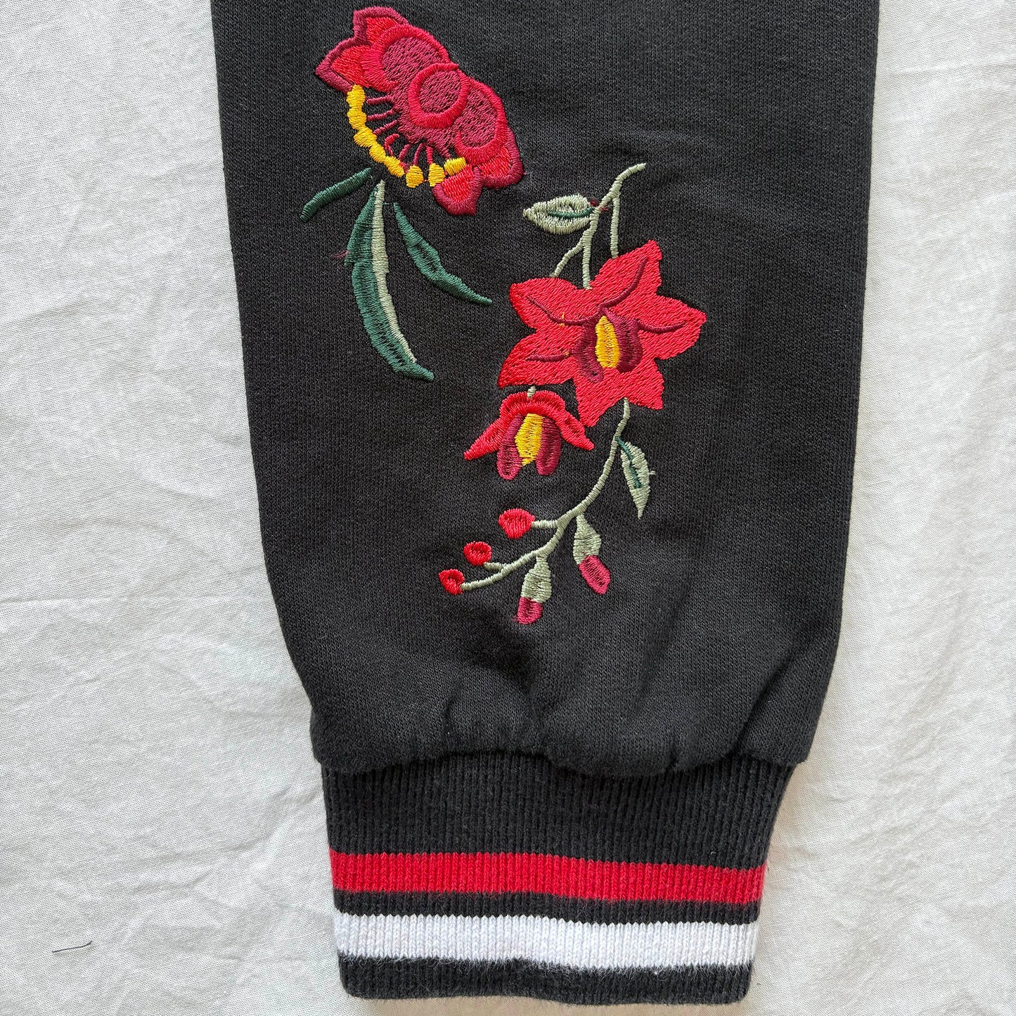 Black sweatshirt sleeve with red floral embroidery on a textured gray background