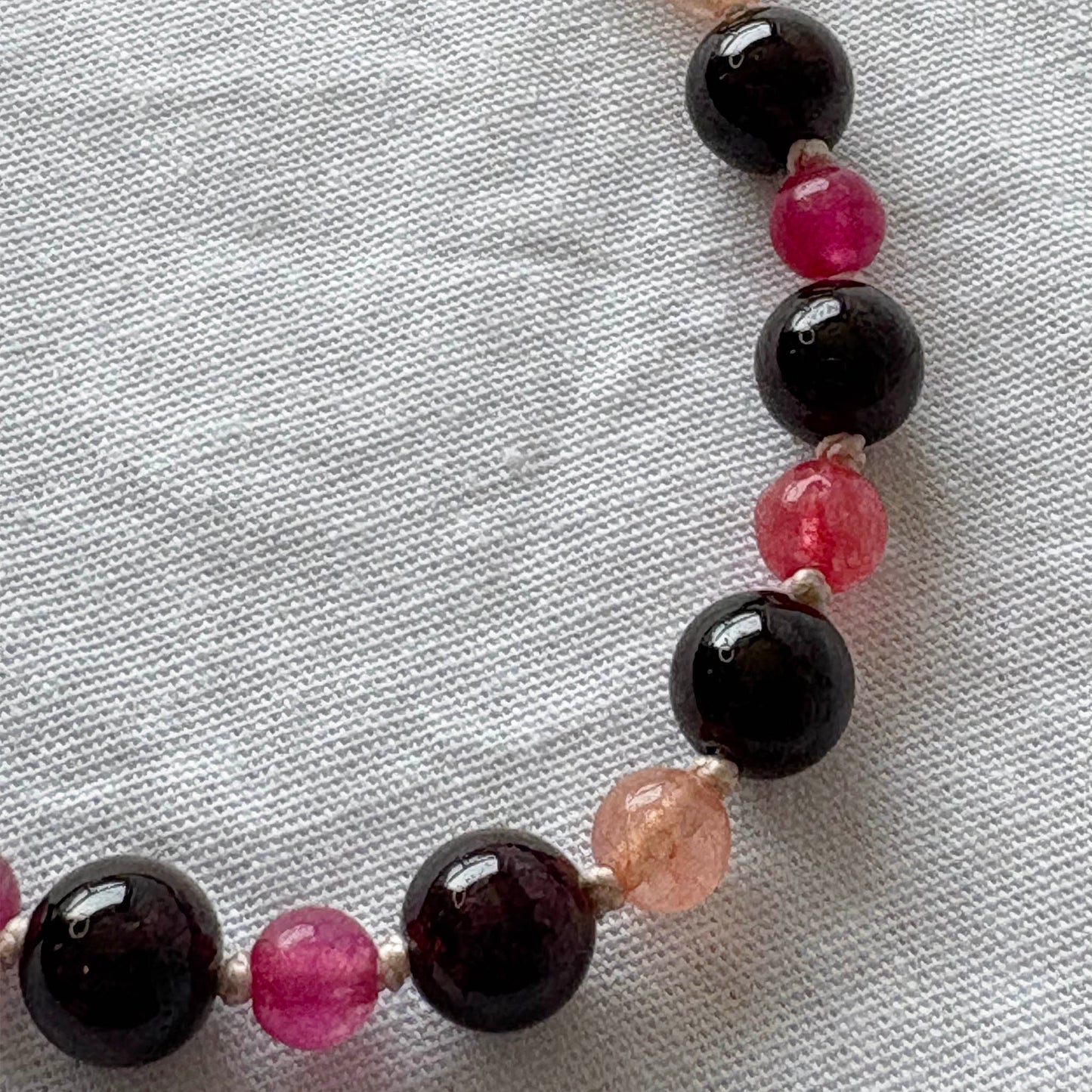 Beaded bracelet with black, pink, and clear beads on a white fabric background