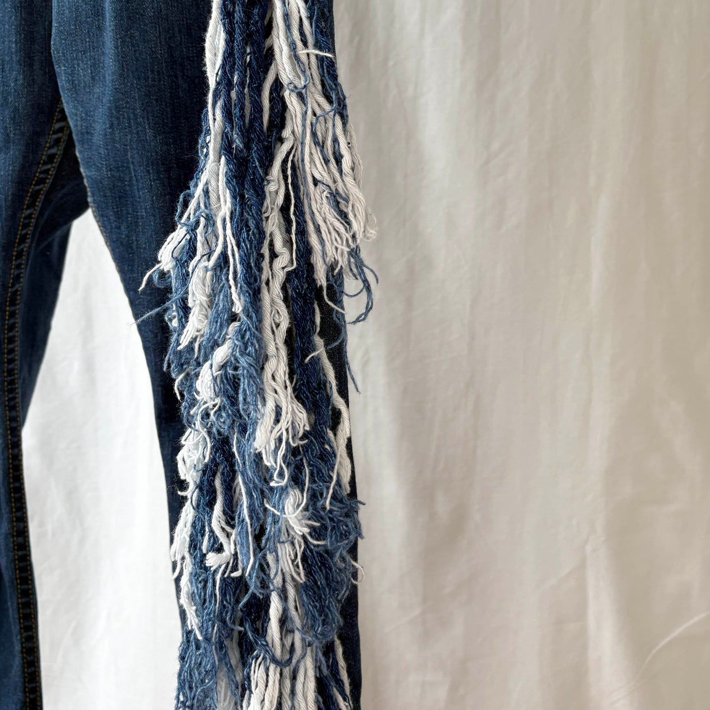 Close-up of a blue and white denim fringed against a neutral background
