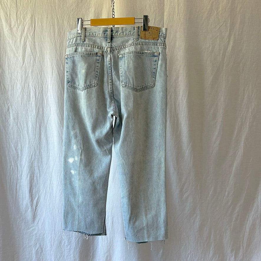 Light blue jeans hanging on a wooden hanger against a plain white background