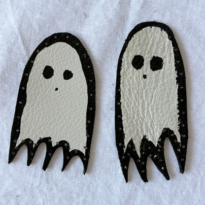Two white ghost-shaped patches with black outlines on a white background