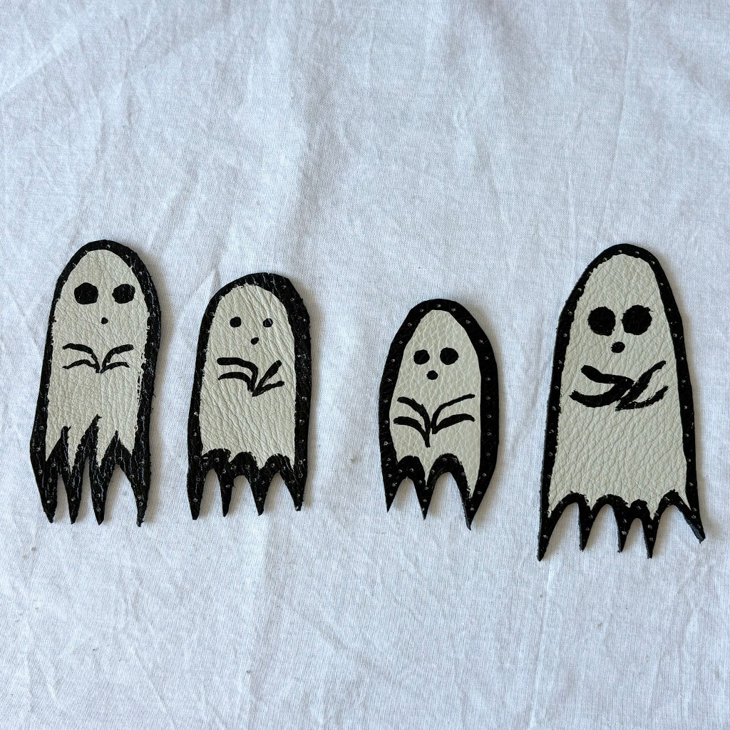 Four black and white ghost-shaped white leather patches with black outlines. on a white surface