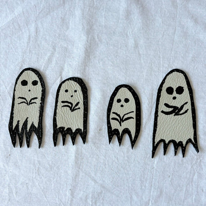 Four black and white ghost-shaped white leather patches with black outlines. on a white surface