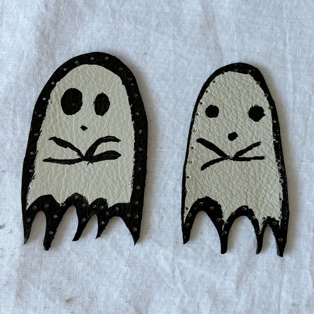 Two ghost-shaped white leather patches with black outlines on a white background