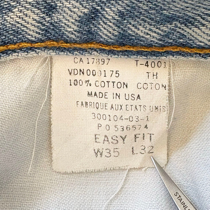 Fabric tag on denim fabric with text and a pair of scissors.