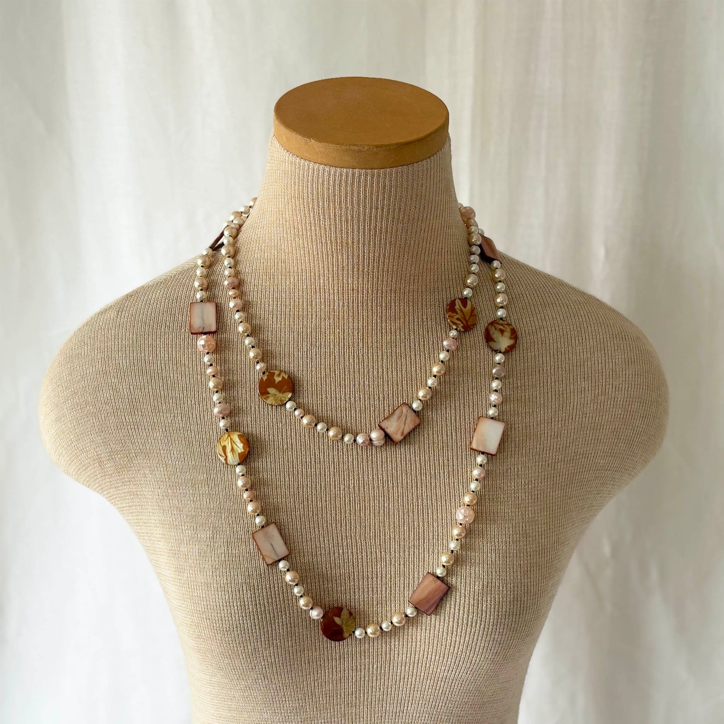 Necklace with pearls and shell and acrylic accents on a mannequin bust against a white background
