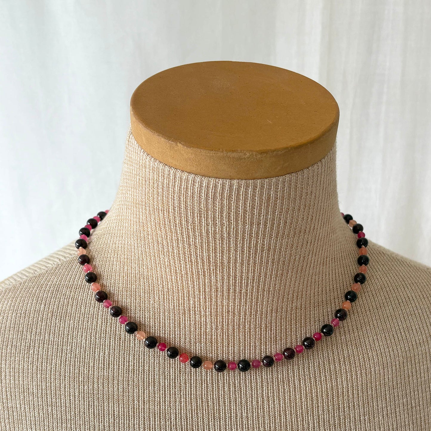 Necklace with black and red beads on a mannequin bust against a white background