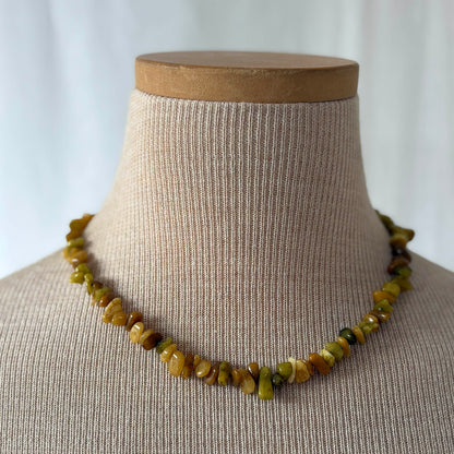 Necklace with green beads on a mannequin bust against a plain background