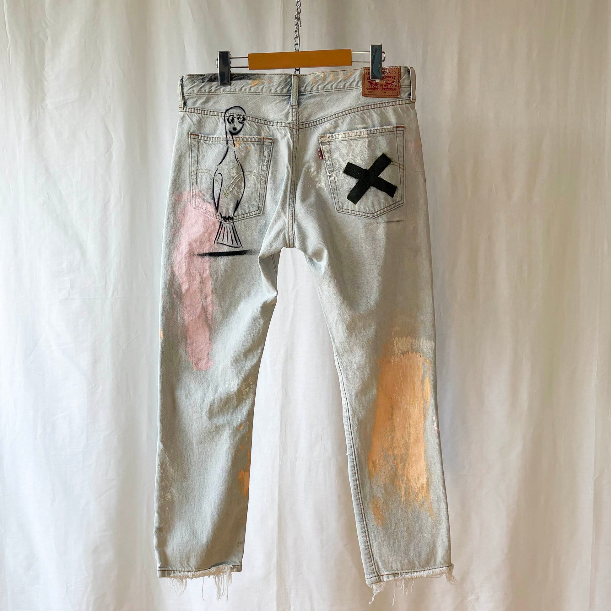 Distressed denim jeans with spray paint stencils on a white background