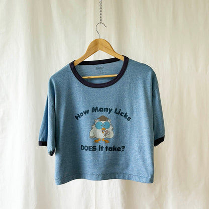 Blue t-shirt with tootsie pop owl graphic and text on a hanger against a white background