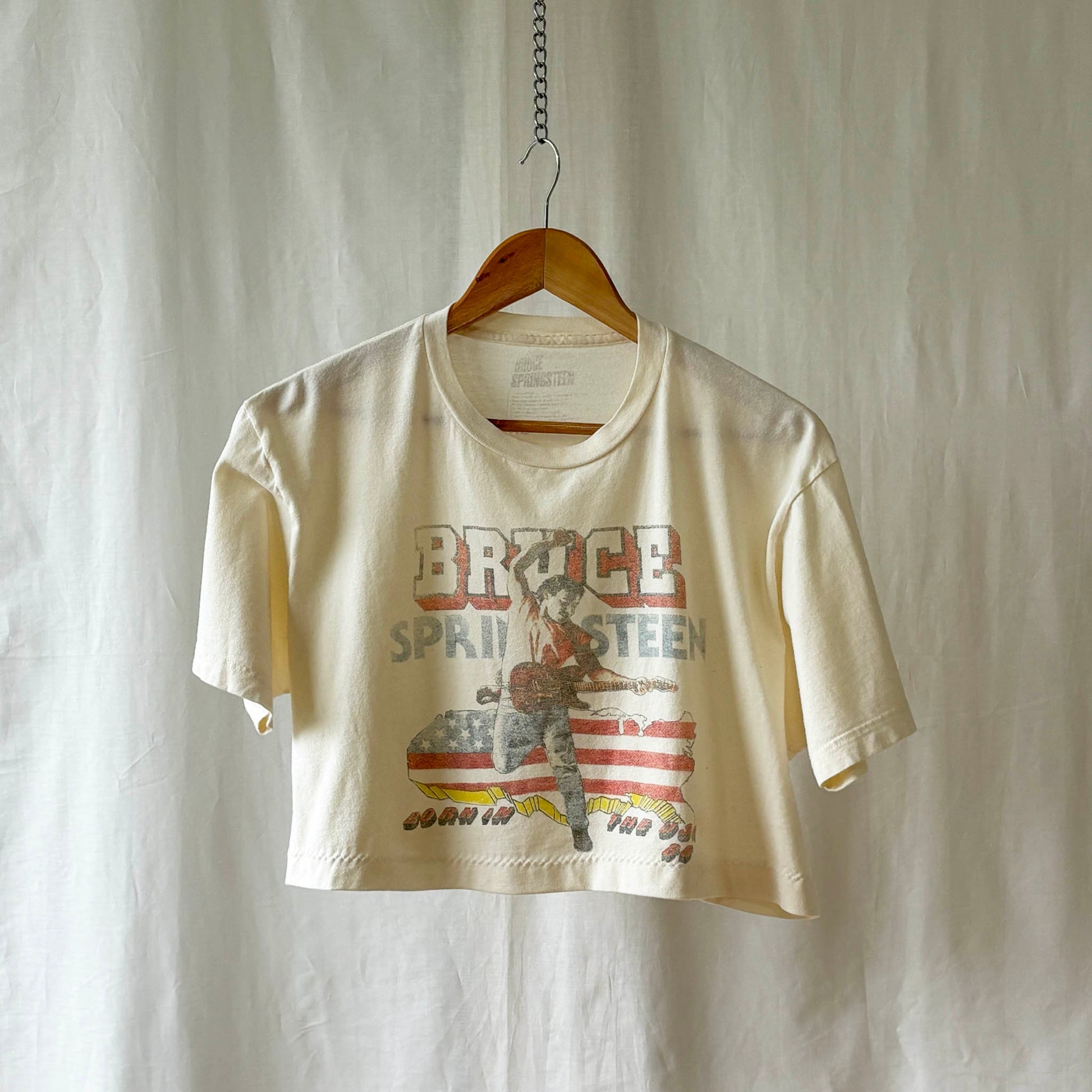 Off white Bruce Springsteen Born in the USA t-shirt  on a wooden hanger against a white background