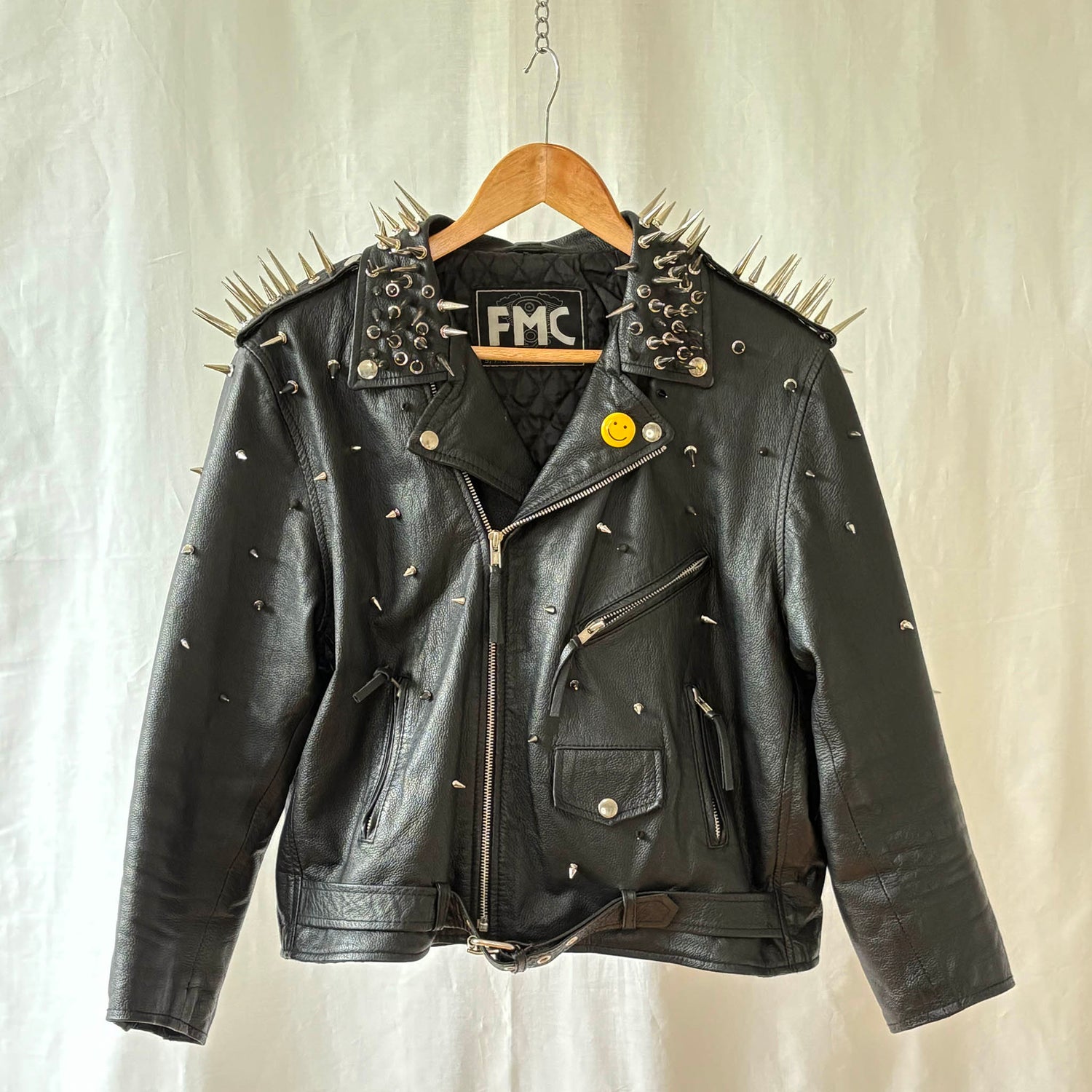 Black leather jacket with spikes on a hanger against a neutral background