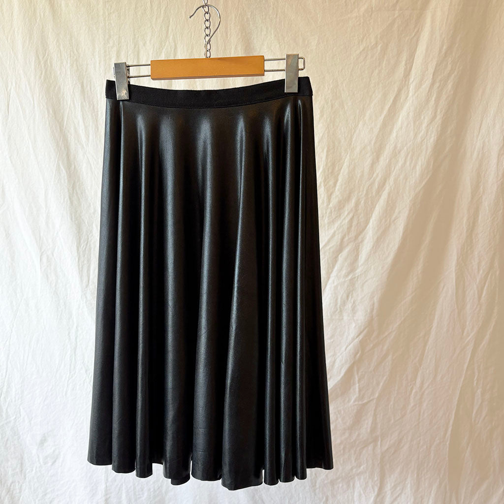 Black wet look spandex skirt on a hanger against a beige background