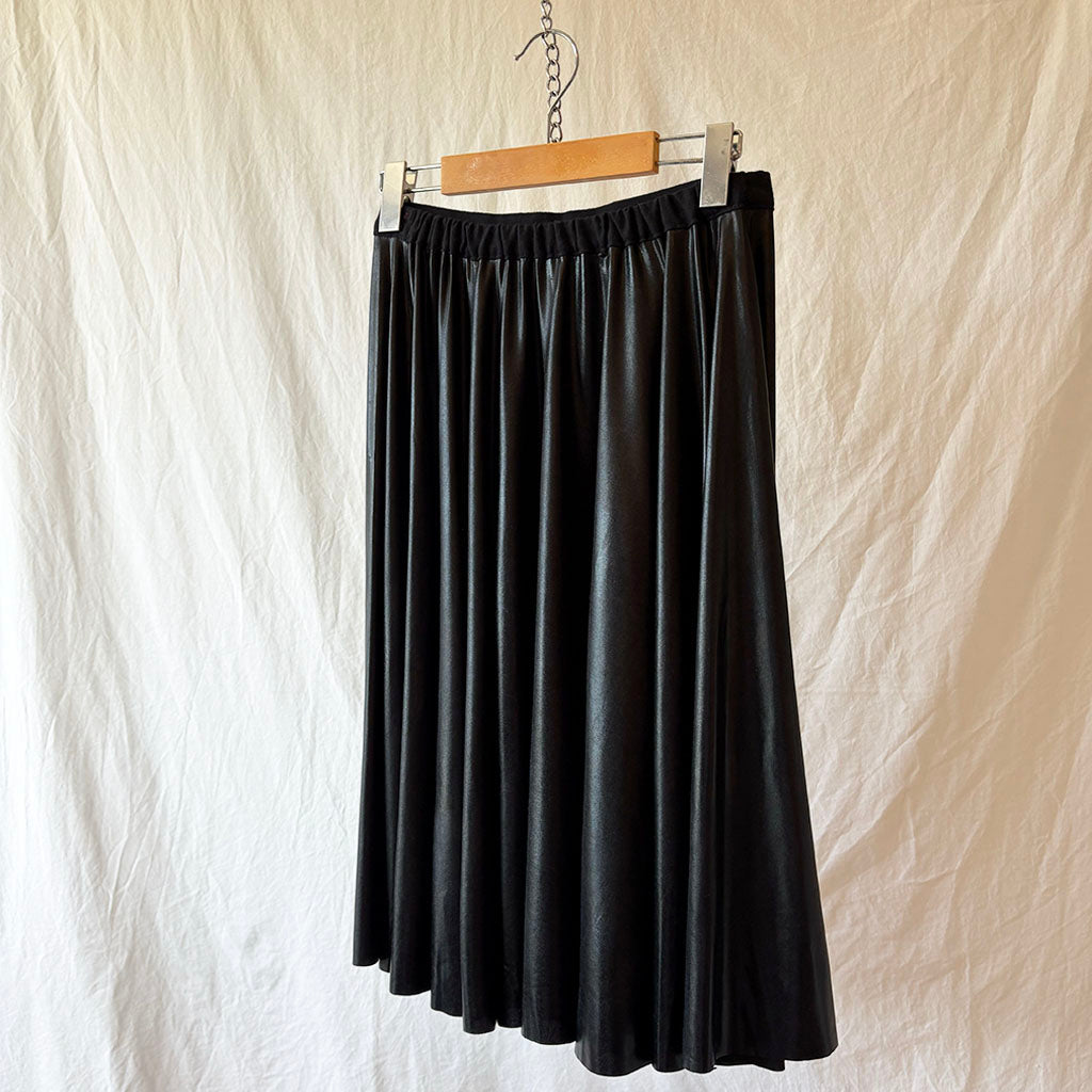 Black wet look spandex skirt hanging on a wooden hanger against a beige background