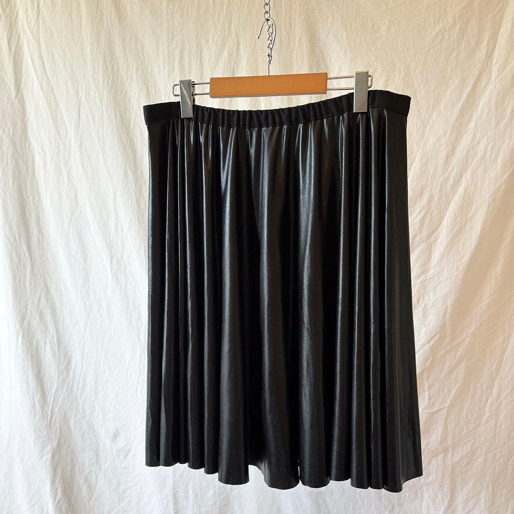 black wet look spandex skirt hanging on a wooden hanger against a beige background