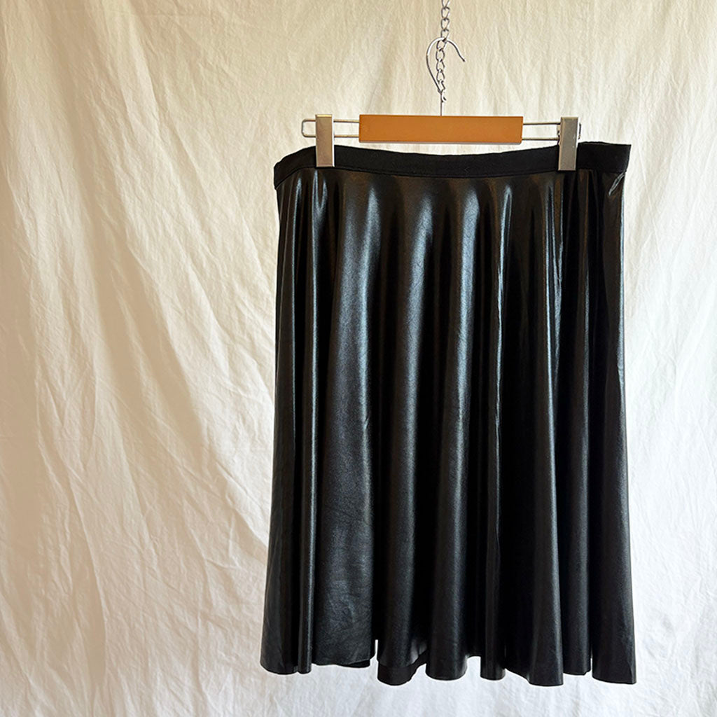 Black wet look spandex skirt on a hanger against a plain background