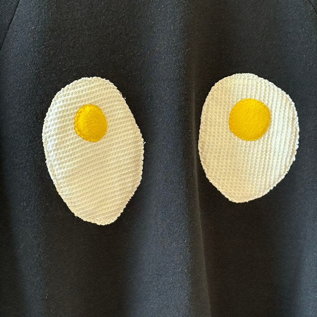 Two quilted eggs with yellow yolks on a dark fabric background