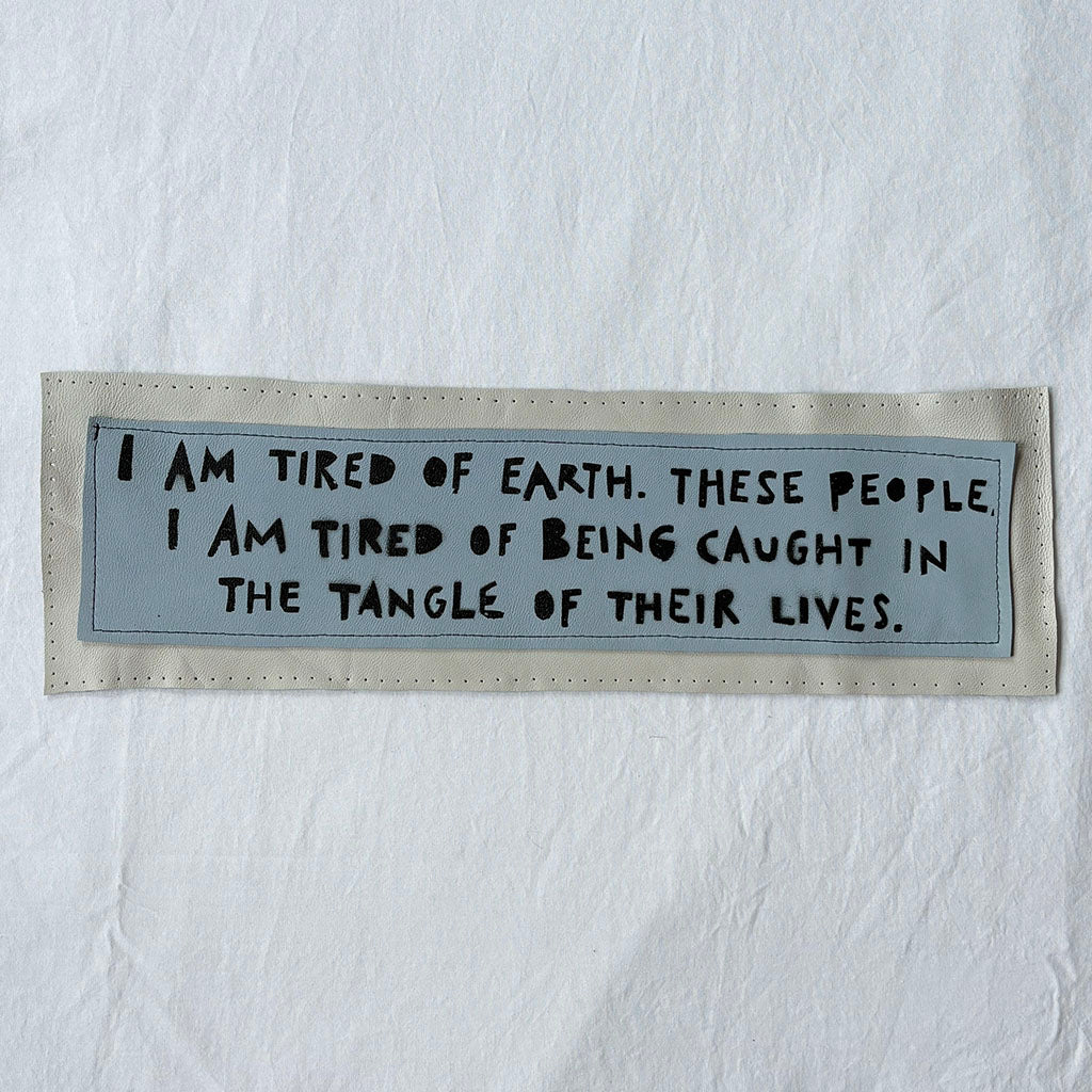 Textile patch with a quote on a white background "i am tired of earth. these people. i am tired of being caught in the tangle of their lives."