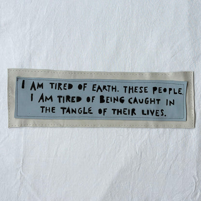 Textile patch with a quote on a white background "i am tired of earth. these people. i am tired of being caught in the tangle of their lives."