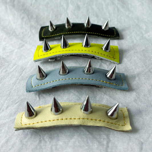 Four leather hair clips with metal spikes on a textured gray background