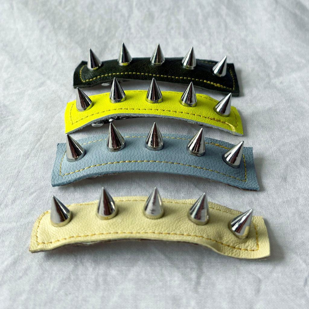 Three leather hair clips with metal spikes on a light gray background