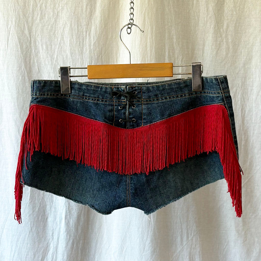 Denim skirt with red fringe on a hanger against a white background