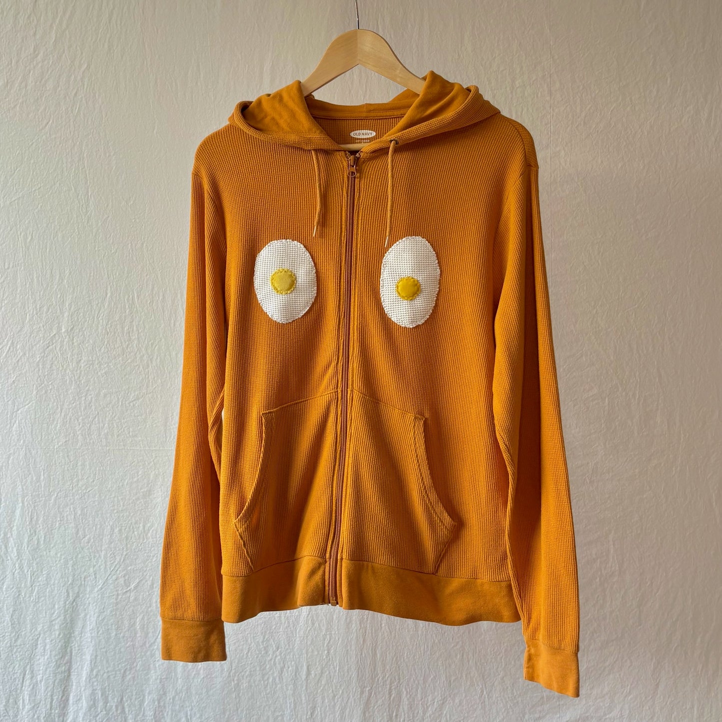 Golden yellow waffle weave zip hoodie with kangaroo pockets and two handmade egg patches on the chest.