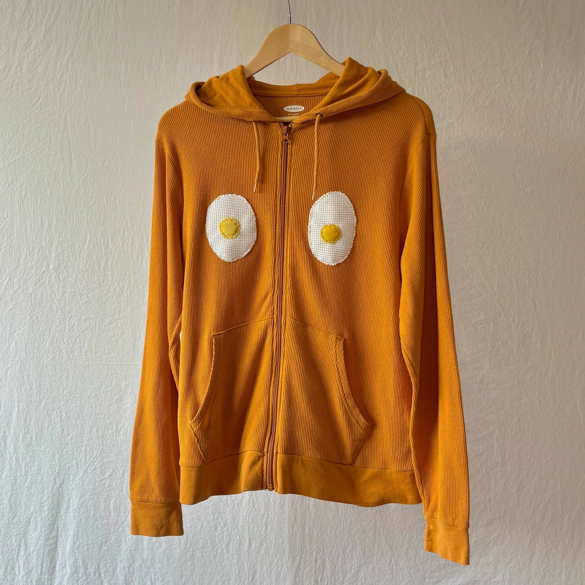 Golden yellow waffle weave zip hoodie with kangaroo pockets and two handmade egg patches on the chest.