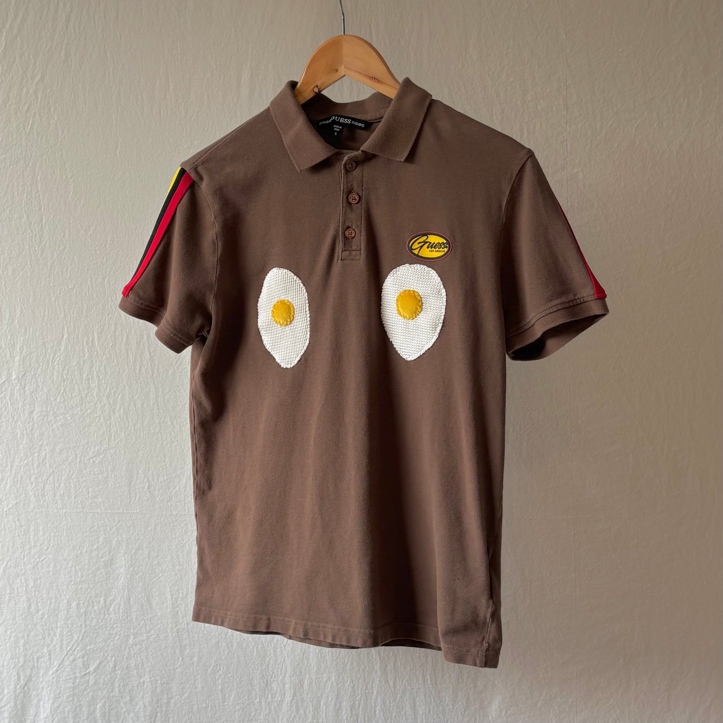 A brown polo shirt with red black and yellow arm striping and two handmade egg patches on the chest