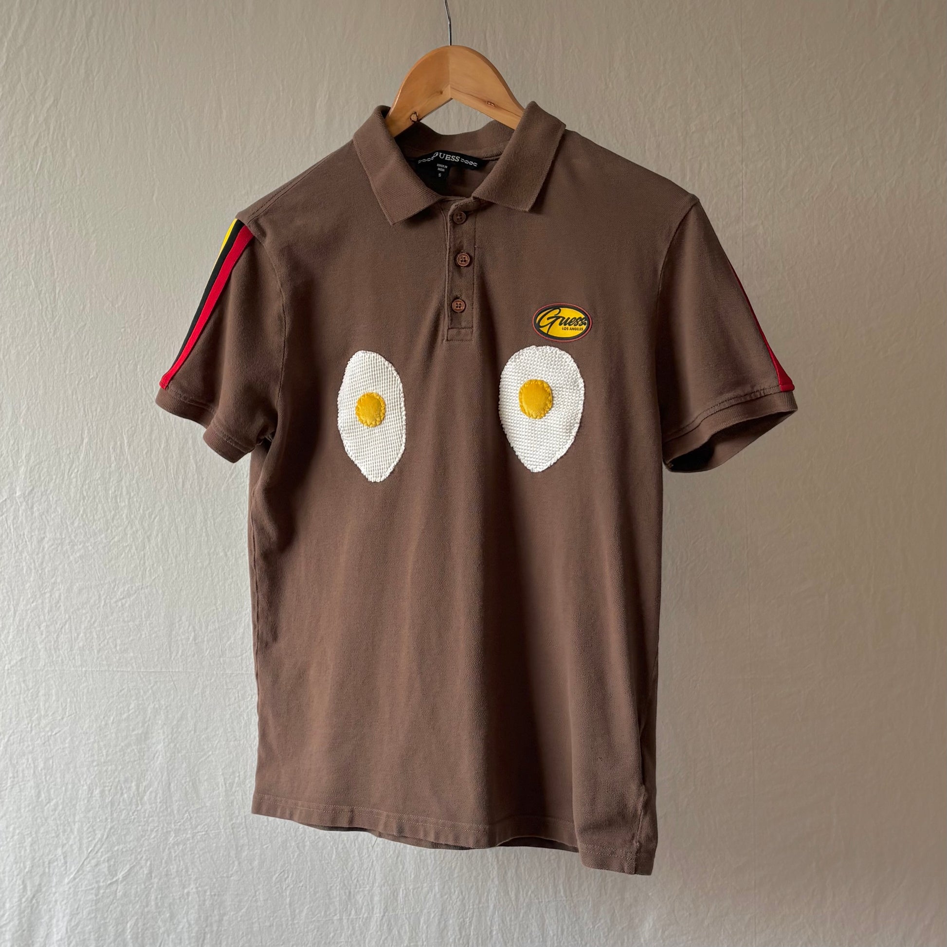 A brown polo shirt with red black and yellow arm striping and two handmade egg patches on the chest