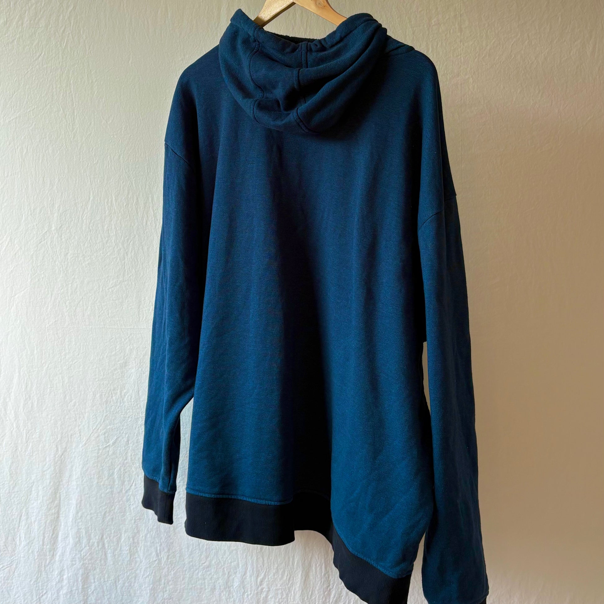A dark blue hooded sweatshirt hanging on a wooden hanger against a textured off-white wall.