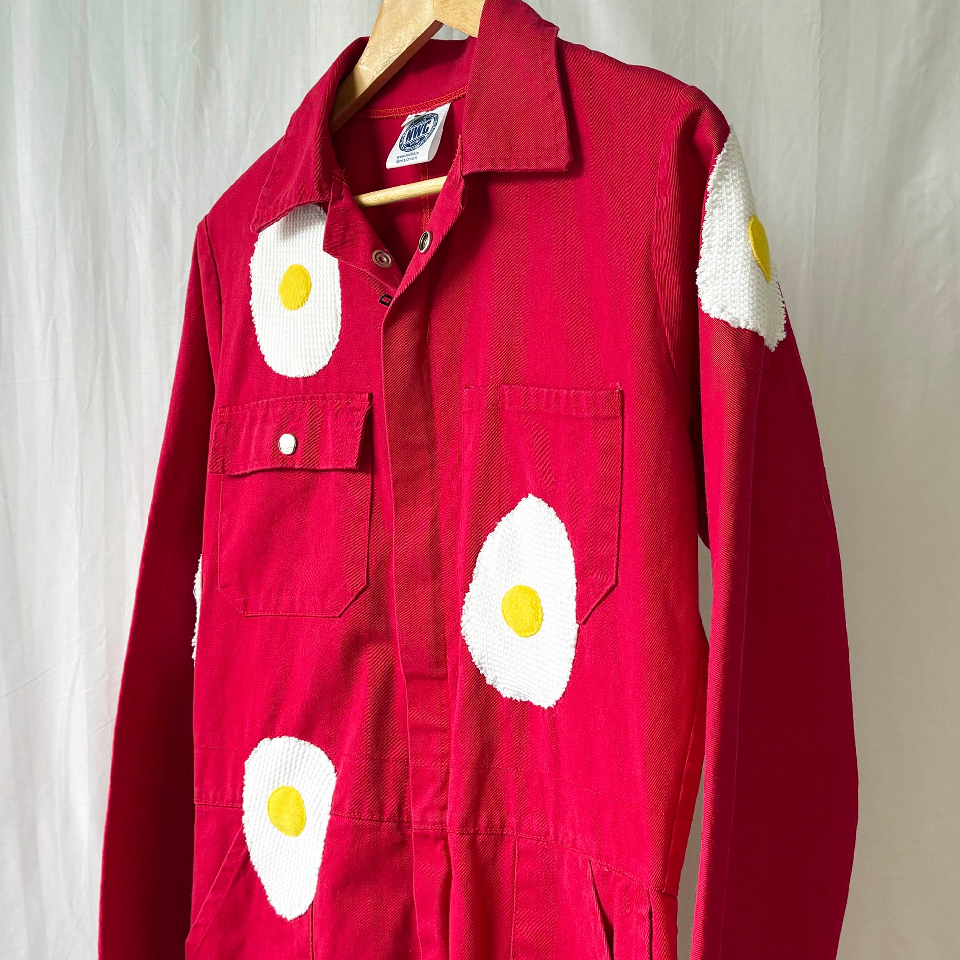 Red jumpsuit with egg design on a hanger against a neutral background