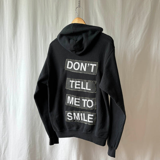 Black hoodie with text on the back, hanging against a neutral background