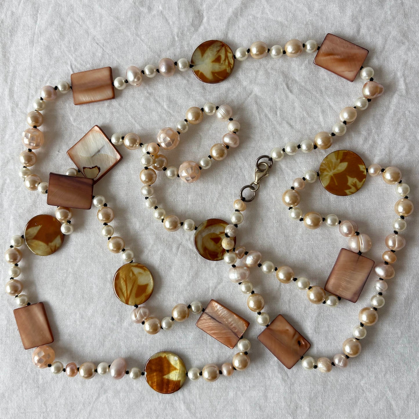 Pearl necklace with shell and acrylic accent beads on a light fabric background