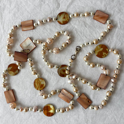 Pearl necklace with shell and acrylic accent beads on a light fabric background