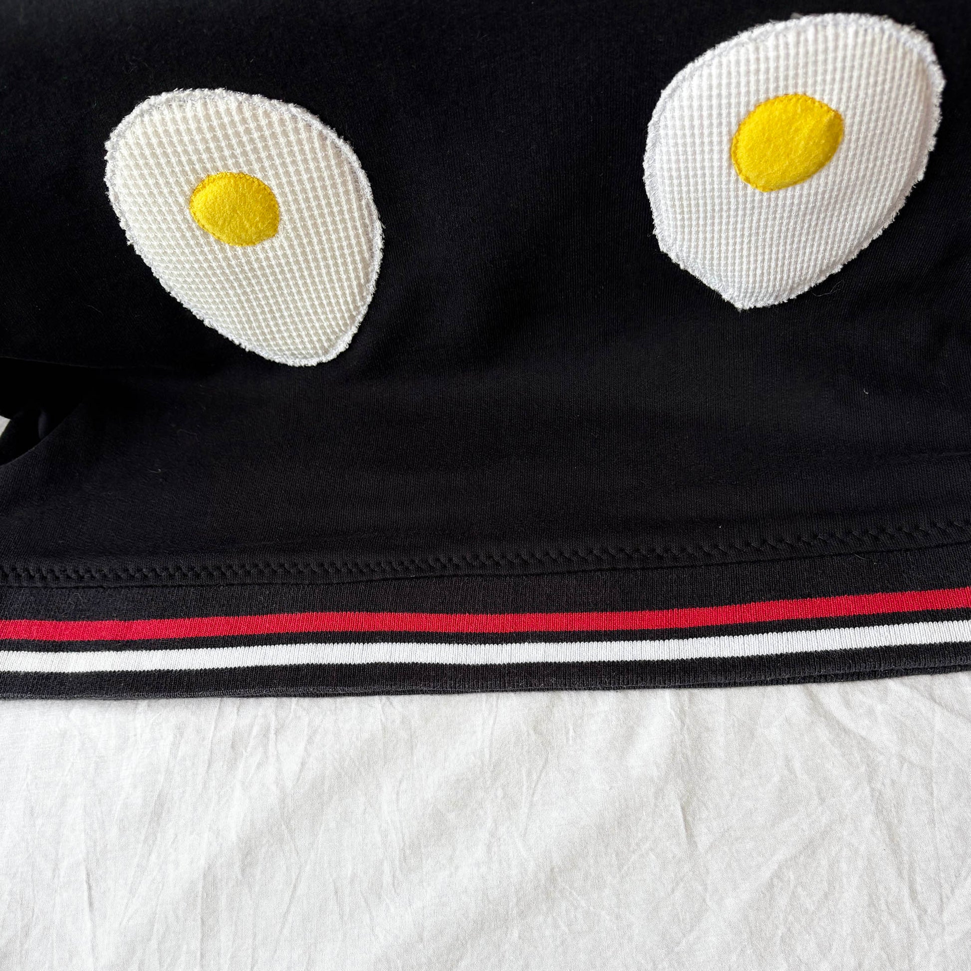 Black hoodie with cartoonish fried egg designs on a white background