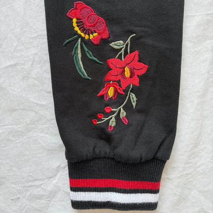 Black sweatshirt sleeve with red floral embroidery on a textured gray background