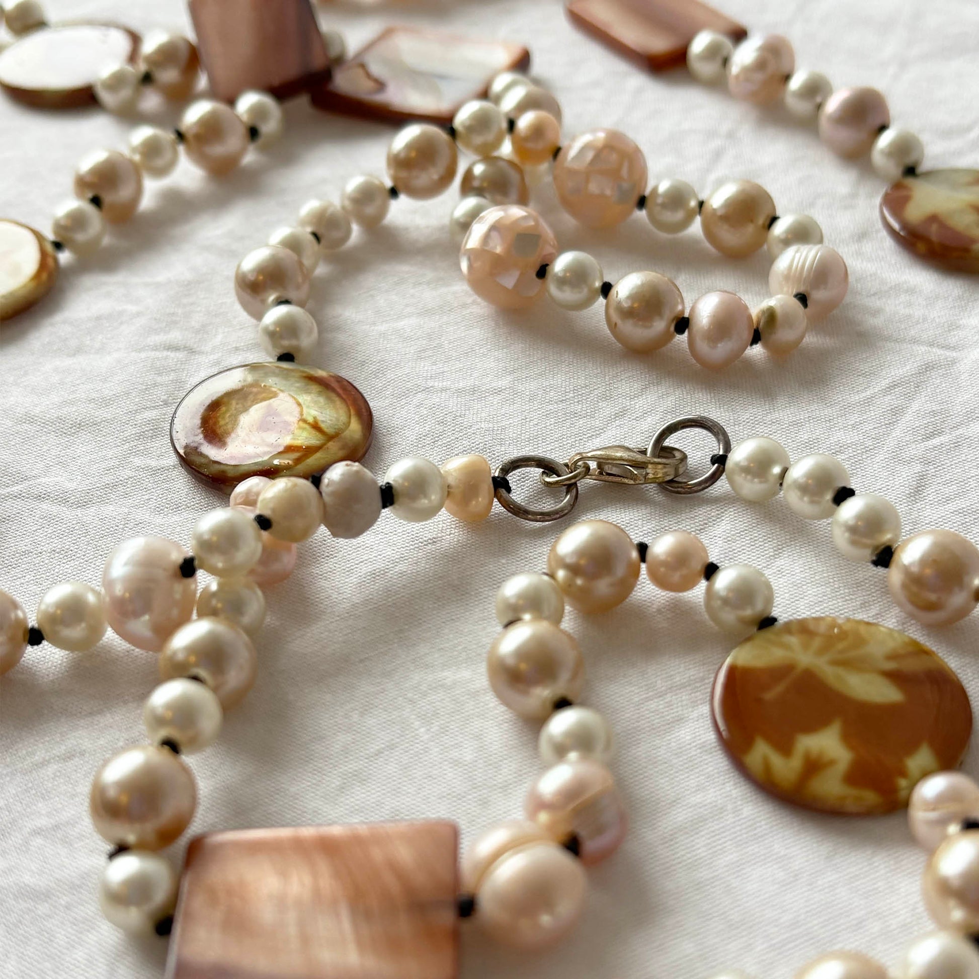 Pearl necklace with shell and acrylic accents on a light fabric background.