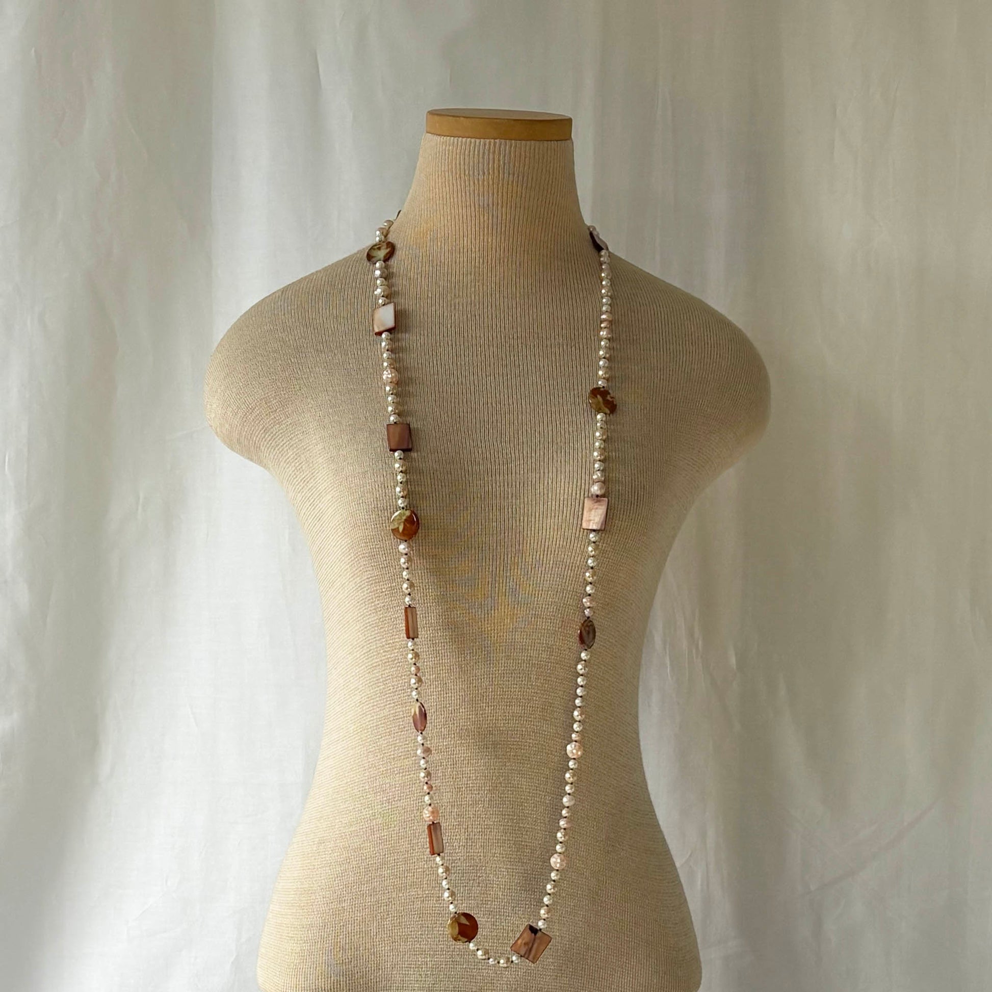 Pink pearl necklace with shell and acrylic accents on a mannequin against a plain background