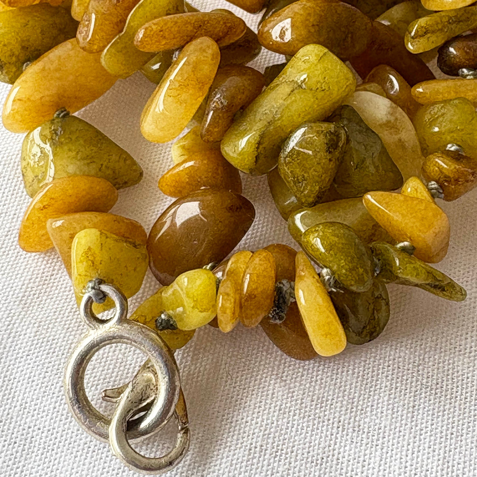 Necklace with yellow and green stone beads and a silver clasp on a white fabric background