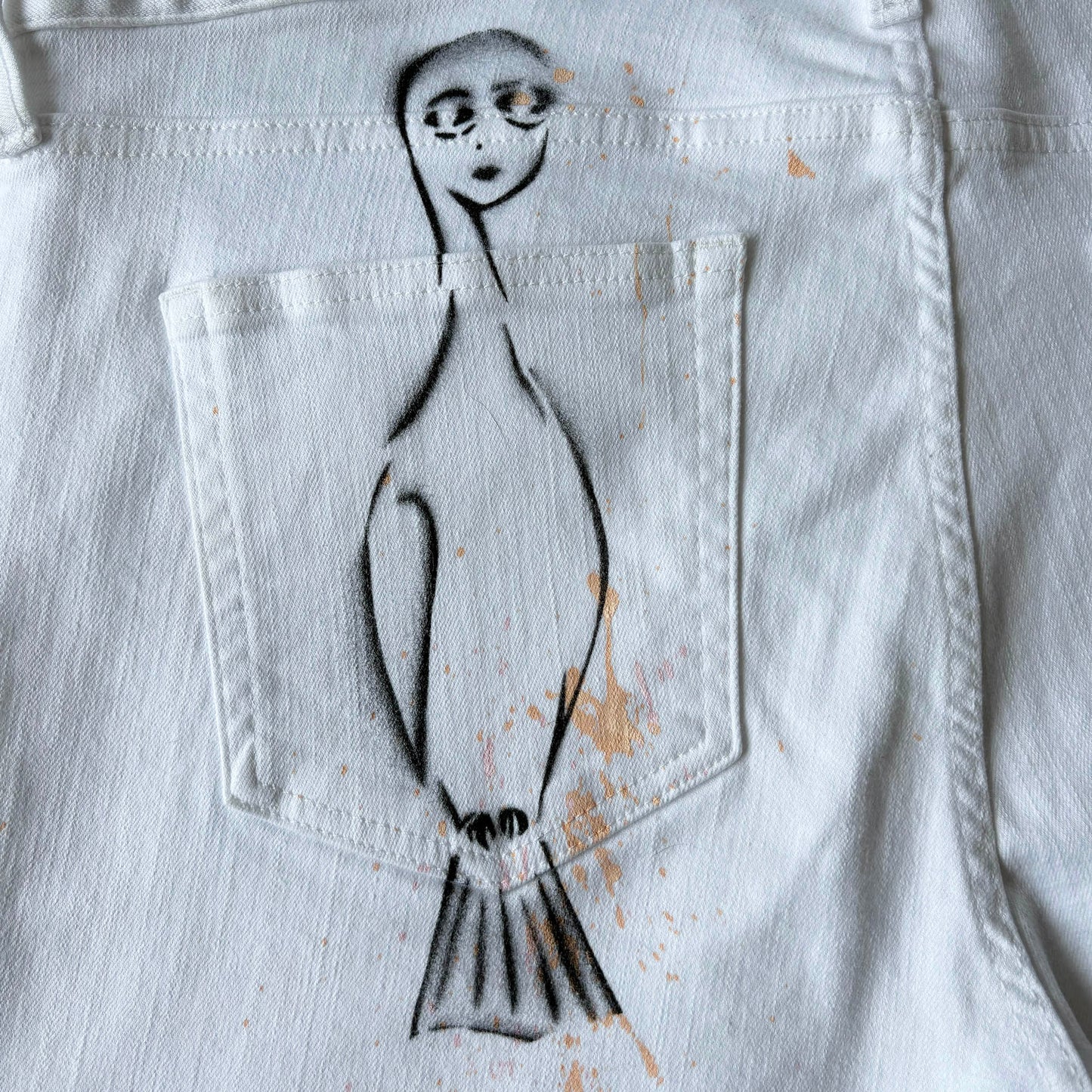 black bird person stencil with peach paint splatter over the pocket of white denim pants.