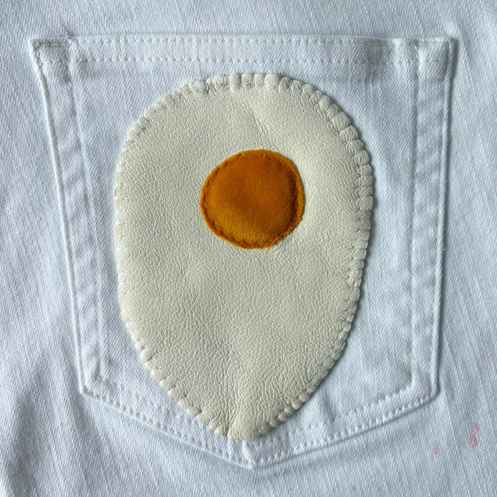 Fabric patch of a fried egg on white denim.