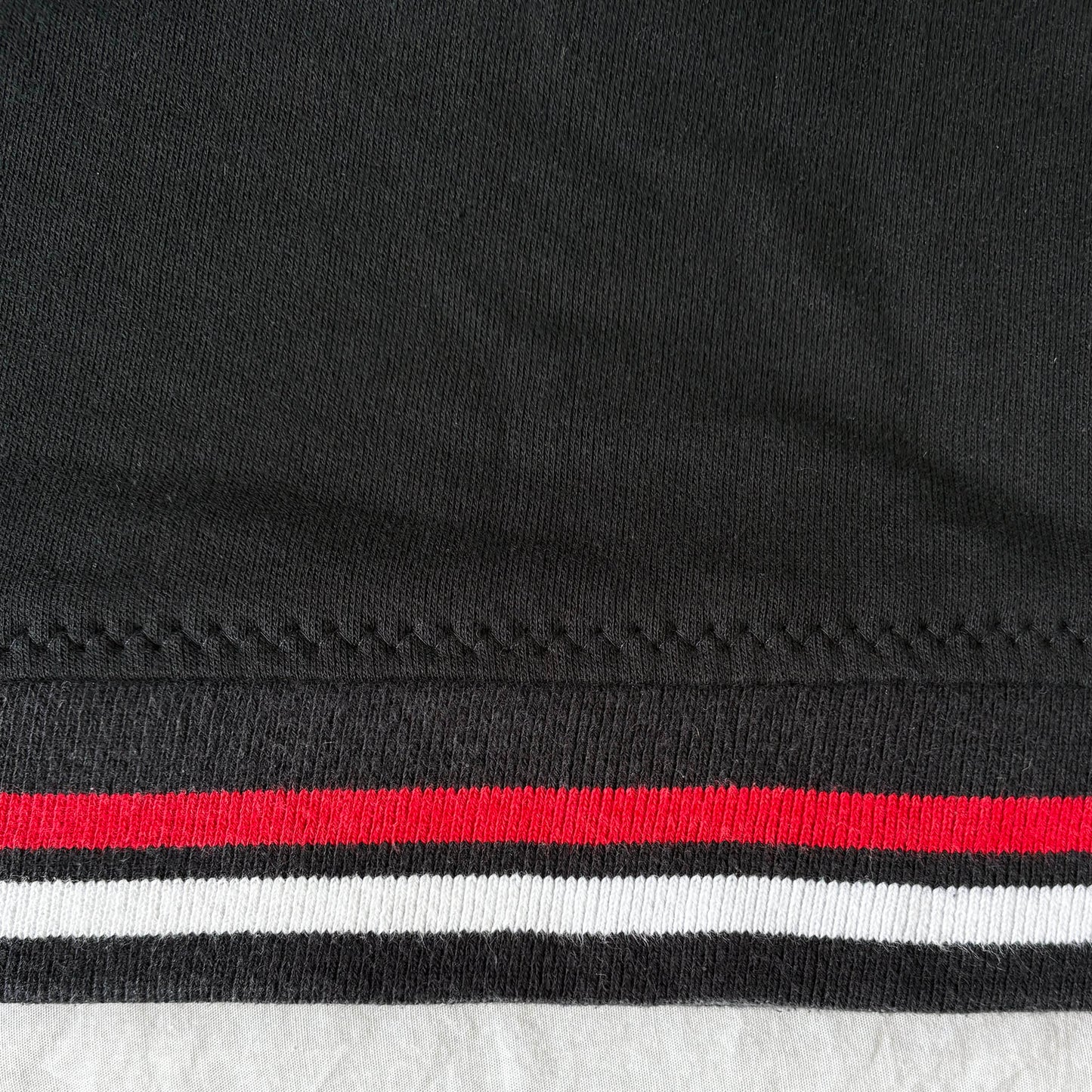 Close-up of reattached hem. hem has red and white stripes on a textured surface