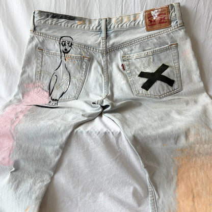 Light blue denim pants with a black 'X' on the pocket and a drawing of a bird person on the back pocket, laid flat on a white surface.