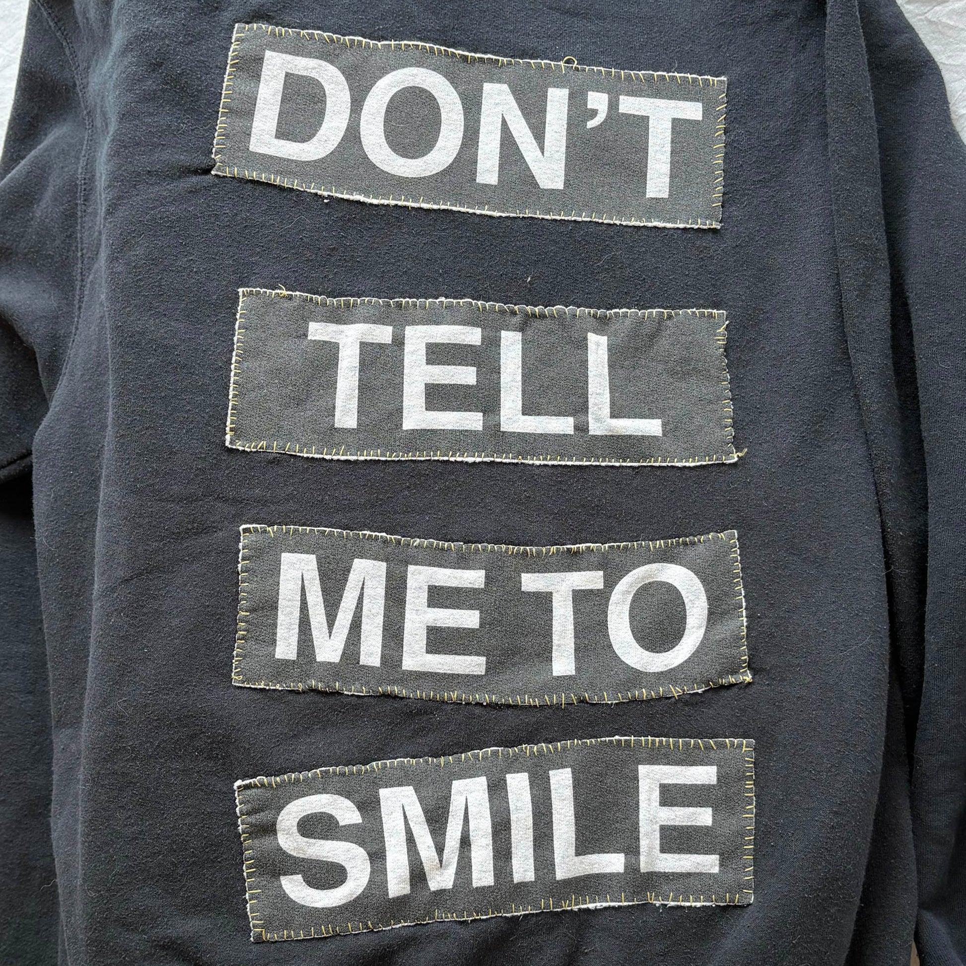 Text on a dark fabric background with motivational message 'Don't tell me to smile.'