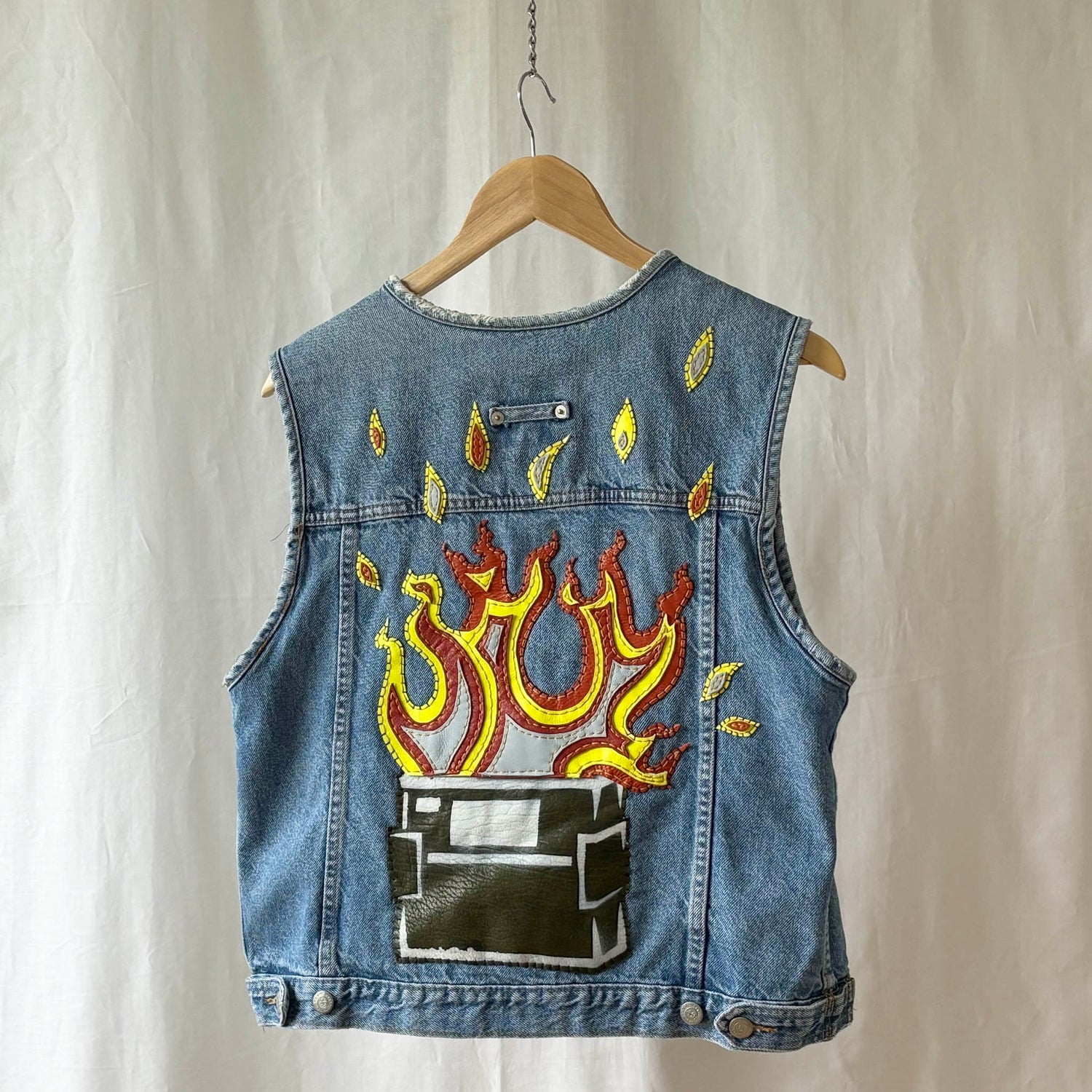 Denim vest with dumpster fire leather back patch on a hanger against a neutral background