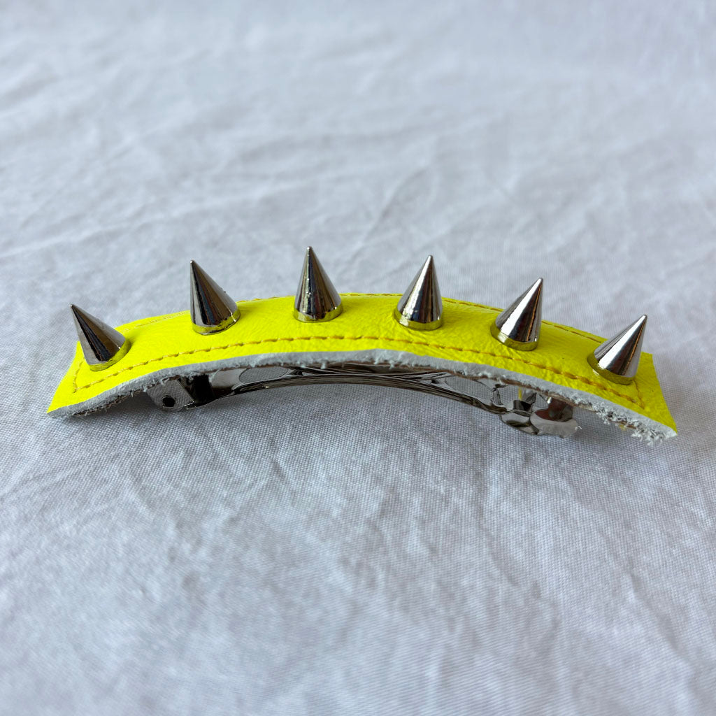 Neon yellow hair clip with silver spikes on a gray background